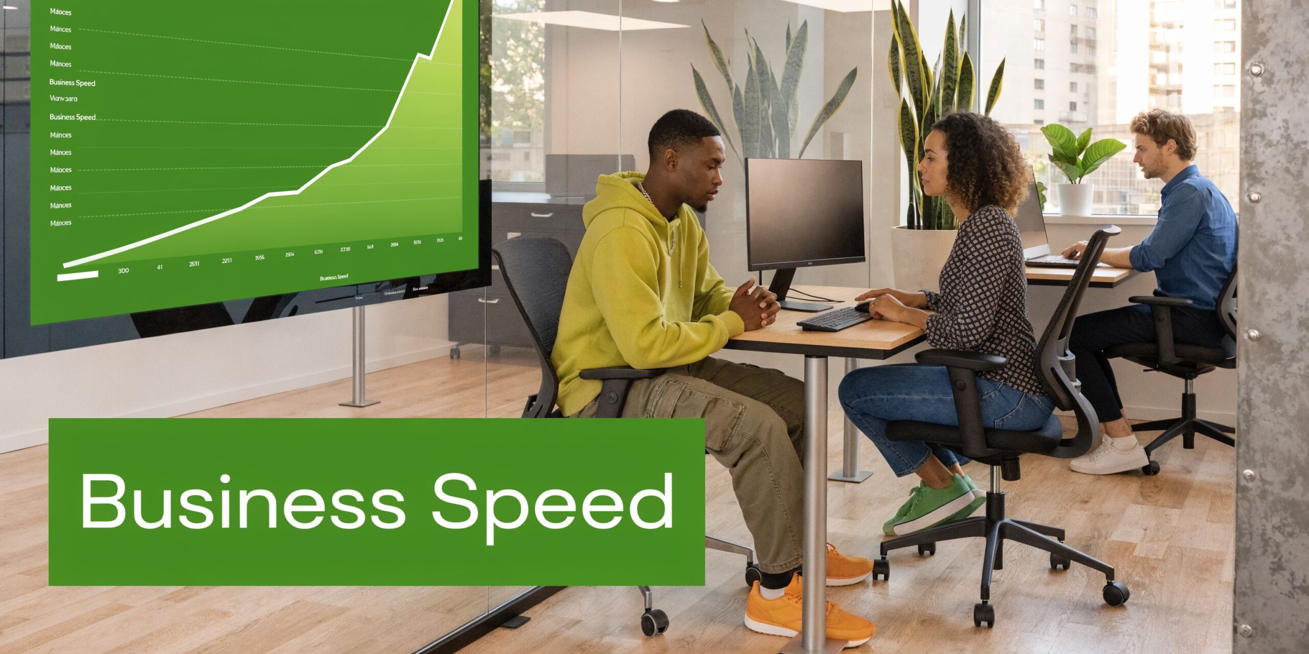 A professional office setting with colleagues working on computers and a large digital screen displaying business metrics.