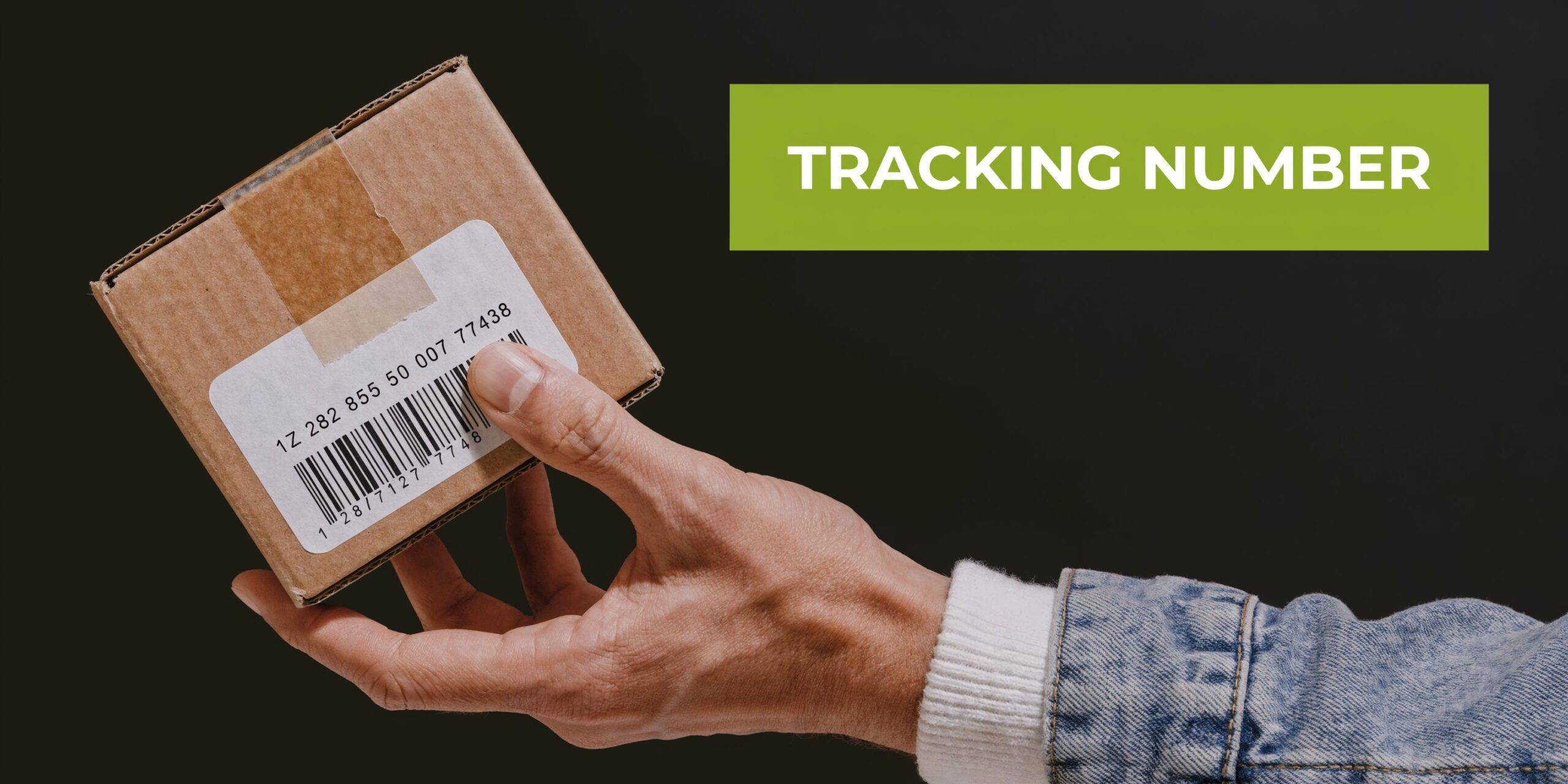 A hand holding a small brown cardboard parcel with a shipping label showing a tracking number.