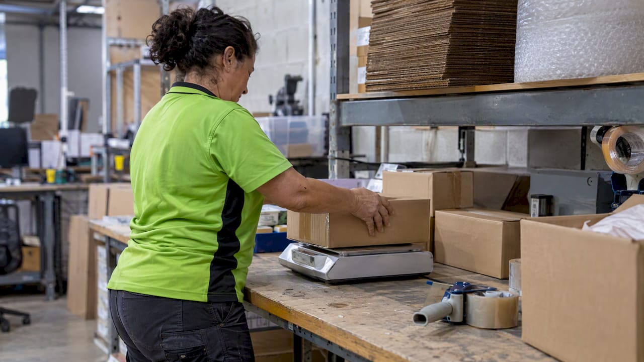 Worker weighing parcel on postal scale